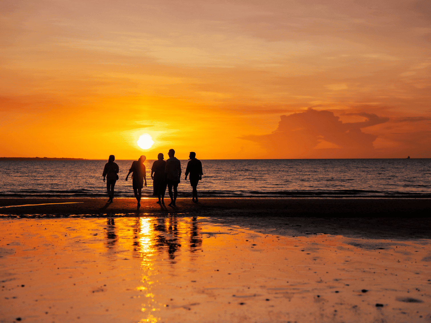 Visitors enjoying a sunset stroll along Mindil Beach, with golden reflections on the shoreline and a colourful tropical sky overhead.