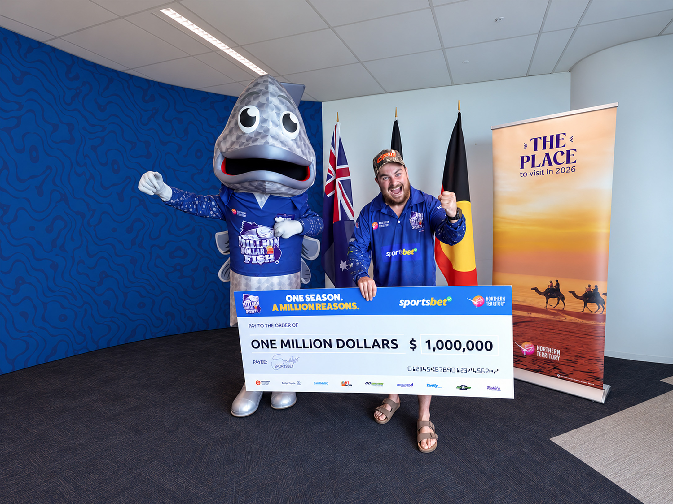 A man standing with a Million Dollar Fish mascot and the man is holding a cheque worth $1Million