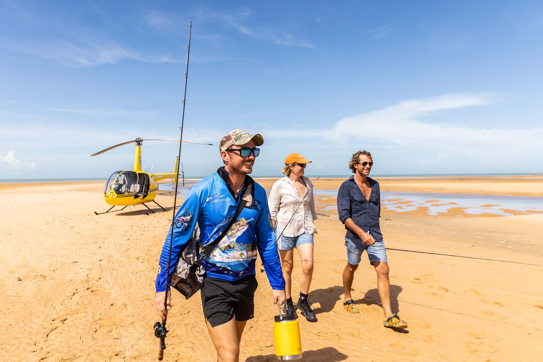 Three people walking on sand with a helicopter in the background