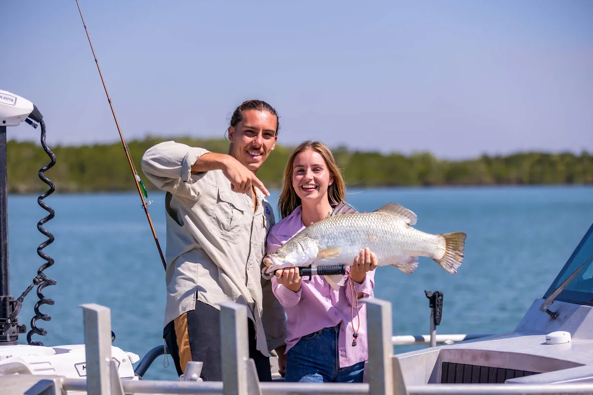 A man and a woman on a boat with the woman holding a fish and the man is pointing at the fish